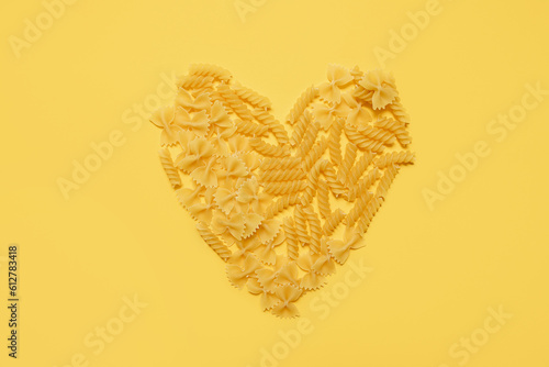  heart made from different types of italian pasta on a yellow background. copy space.