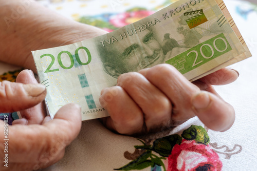 A Swedish pensioner holds a bunch of low denomination banknotes in her hands, Cost of living for a senior in Sweden, Pensions and the Swedish social system for the elderly