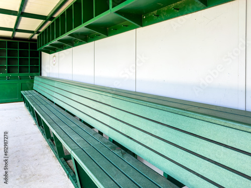 typical nondescript high school baseball, softball dugout with green bench and gray walls. No people visible. Not a ticketed event. 
