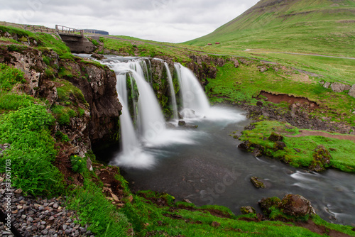 Vue sur une chute d'eau dans une rivière avec une vallée en arrière plan recouverte de gazon vert
