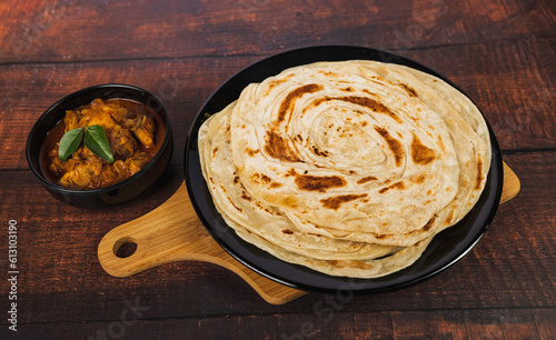 Kerala Parathas or Porotta Roti with red spicy chilly chicken. Barotta naan is a layered flatbread made from maida whole wheat flour. Indian food on a wooden table.
