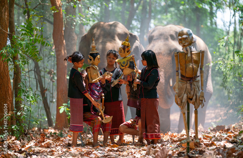 Group of Asian boys and girl enjoy to show or practice manipulate the puppets in front of big elephant in walkway in jungle and they look happy for this traditional culture.