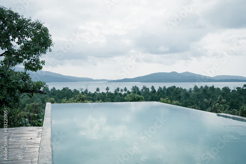 Wide angle view of a beautiful infinity pool in a tropical island overlooking the sea and other islands of exotic archipelago. Overcast day, almost sunset, water reflections.