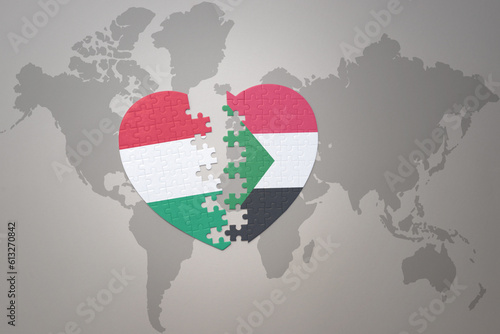 puzzle heart with the national flag of sudan and hungary on a world map background.Concept.