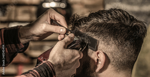 Bearded man in barbershop. Haircut concept. Man visiting hairstylist in barbershop. Barber works with hair clipper