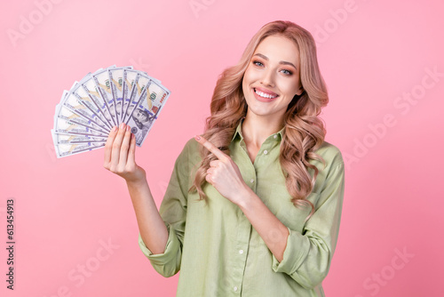 Portrait of cheerful successful person direct finger hand hold dollar bills isolated on pink color background