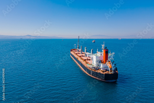 Bulk vessel for dry cargo in anchorage in sea waiting loading in industrial port, aerial shot