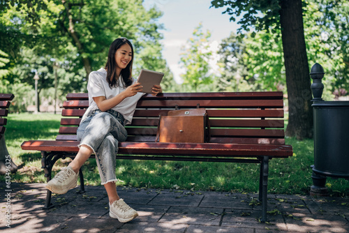 Young Japanesse woman using digital tablet while resting in the park