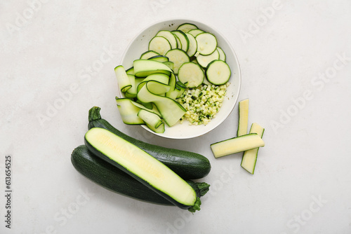 Bowl with slices and fresh green zucchini on white background