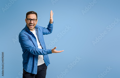 Cheerful businessman demonstrating something with copy space while standing on blue background