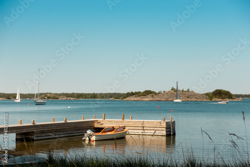 Stockholm archipelago in sunset with small boat moored to pier with sailing boats anchored in background