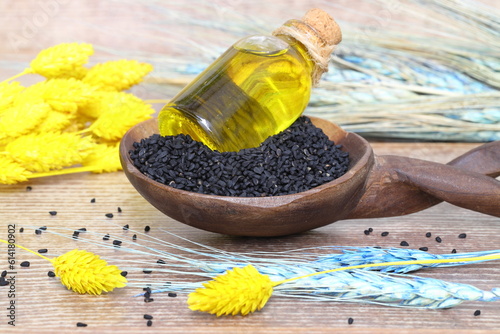 Black cumin seeds and essential oil with bowl and wooden shovel or spoon. Nigella Sativa in glass bottle. Organic herbal medicine for many diseases