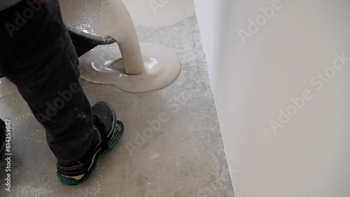 A male worker working with self-levelling cement mortar during a floor repair. A worker pours a bucket of mortar to level the floor. Self-levelling concrete floor mix.