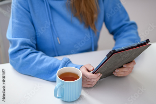 Młoda dziewczyna z kubkiem herbaty w ręce korzysta z tabletu