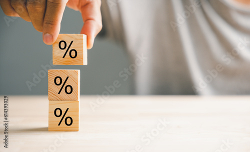 Concept of interest rate and financial rates. Hand placing a wooden cube block on top, symbolizing an increasing trend, with an upward direction icon and percentage symbol.