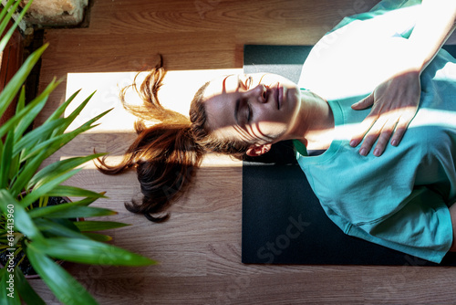 Yoga breathing exercise, serene woman lying down on exercise mat on back with closed eyes and meditating.