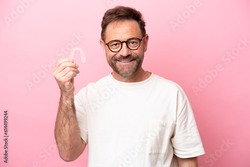 Middle age man holding invisible braces isolated on pink background smiling a lot