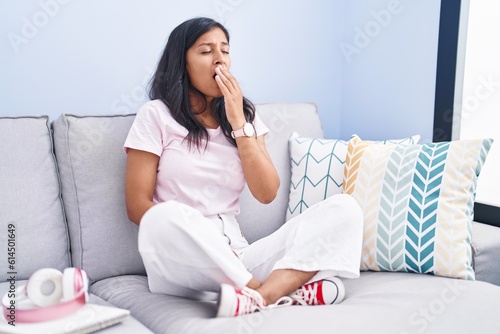 Young hispanic woman sitting on the sofa at home bored yawning tired covering mouth with hand. restless and sleepiness.