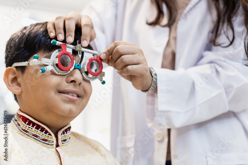 Happy Indian child boy examining eyesight modern ophthalmology equipment in clinic. Patient kid male checkup iris examines ophthalmological hospital. measure eye glasses.