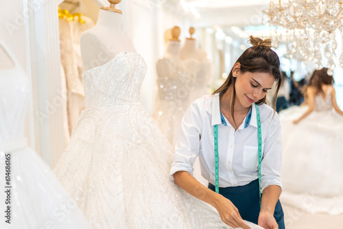 Portrait of entrepreneur bridal shop owner business woman fashion designer stylish working.Attractive designer girl using tape meter fitting on wedding dress with mannequin at wedding studio