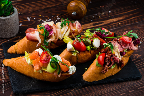 Bruschetta with beef slices, capers, cherry tomatoes, mozzarella, salmon, cucumber, lettuce on a board.