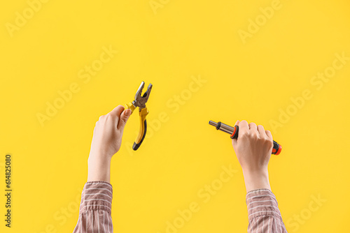 Female hands holding pliers and ratchet screwdriver on yellow background