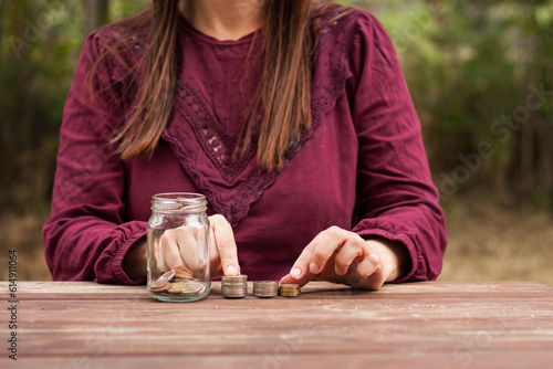 manos de mujer con monedas en mesa de madera con camiseta granate en el campo