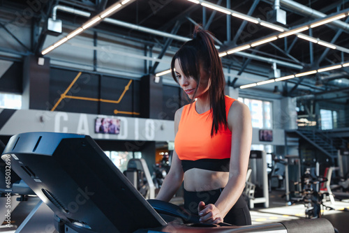 Adult sporty woman workout on treadmill in modern fitness gym. Lady brunette running in interior sports center, exercises treadmill. Cardio working out and sport training concept. Copy ad text space