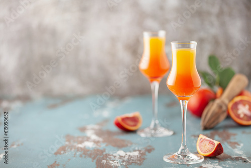 Arancello in grappas wineglass, sweet Italian blood orange liqueur, traditional strong alcoholic drink and blood oranges on the light blue wooden background.