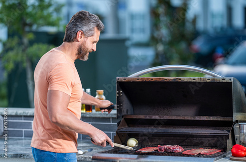 man with hot grill at a barbecue party. Talented barbecue enthusiast. man grilling delicious barbecue on a summer day. man preparing grilled food at backyard barbecue. rib eye steak