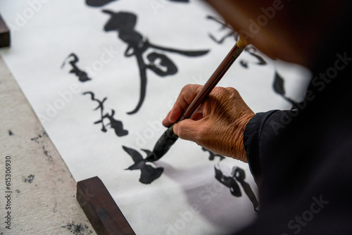 An old Chinese calligrapher is writing brush characters, creating Chinese calligraphy works. Translation: Spring comes, the god of wind arrives.