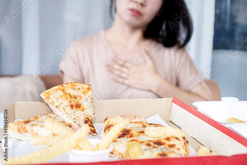 Asian woman having chest and stomach pain after overeating pizza, heartburn from acid reflux caused by GERD