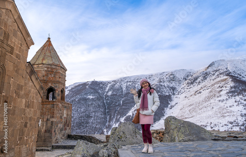 woman tourist standing near Gergeti Trinity Church with the view of snowy Caucasus mountains in winter in Kazbegi, Georgia.