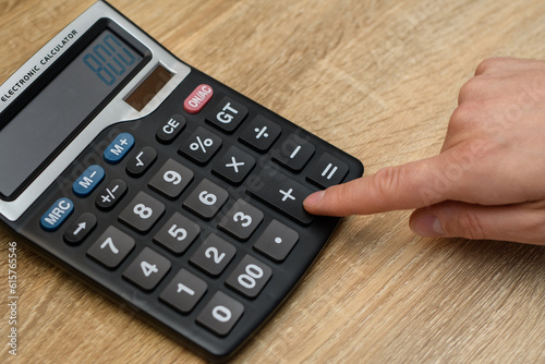 Mężczyzna liczący wydatki na kalkulatorze, który leży na biurku 