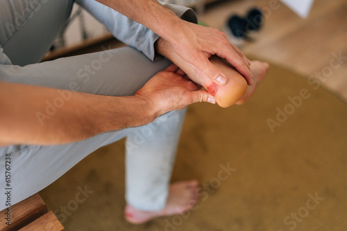 Closeup of unrecognizable man holding foot with pain on sole of foot, massaging blister on foot with fingers. Male suffering from pain due to callus on heel of foot.