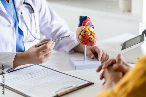 Cardiology Consultation treatment of heart disease. Doctor cardiologist while consultation showing anatomical model of human heart with aged patient talking about heart diseases.