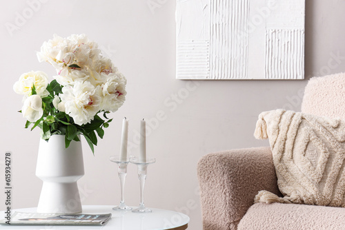 Vase of white peonies with coffee table and armchair near grey wall
