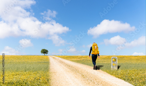 Camino de Santiago - A young pilgrim with a yellow backpack, walking alone in the barren and impressive Spanish plateau, on a pilgrimage to Santiago de Compostela - Selective focus