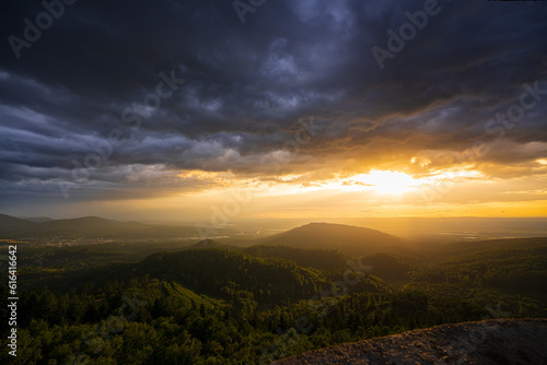 A threatening storm cloud passes over the Murg valley in the northern Black Forest while in the background the setting sun shines in a pleasantly warm light.