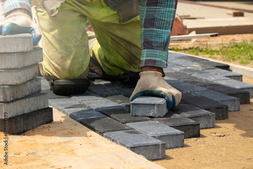 A worker laying paving stones at a sidewalk construction site, close up Pracownik układający kostkę brukową na placu budowy chodnika, z bliska