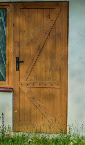 Brązowe drewniane drzwi z czarna klamka i ozdobnymi listwami 
