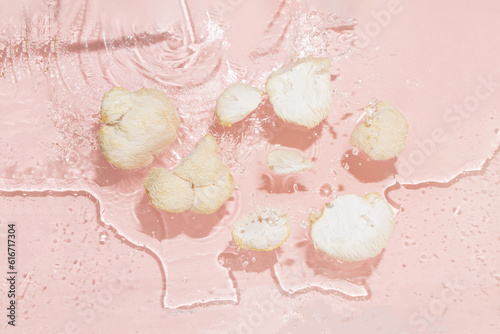 Pieces of lion's mane floating in water. Isolated pastel pink background with splashes. Summer food concept. Flat lay. Top view. Edible medicinal mushrooms hericium erinaceus. Sun and shadows.