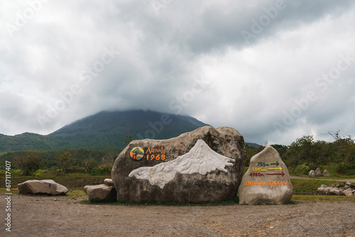 Rocks with sign of arenal 1968 trail and directional arrows in front of mountain volcano covered in clouds at Costa Rica