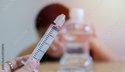 Asian child boy having stuffy nose,difficulty breathing,nasal wash,nose cleaning with syringe and saline. Selective focus at syringe.