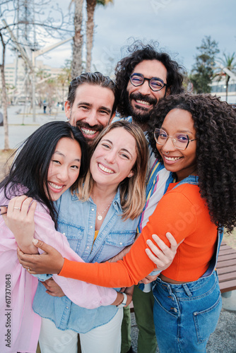 Vertical portrait of group of joyful young adult friends hugging each others. Happy smiling multiracial people embracing and laughing together on a social gathering. Community, union and friendship