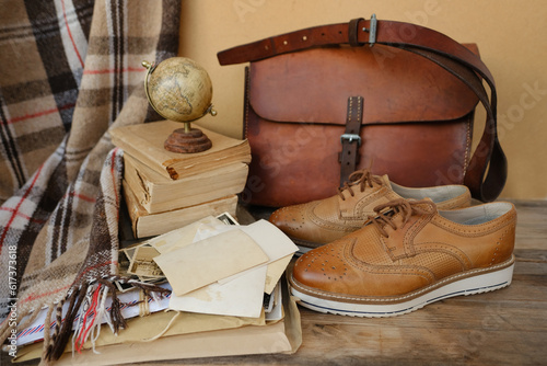 old nostalgic sentimental things, family vintage photographs, stack of books, shoes, leather military satchel on table, checkered grandmother's plaid, family tree, home archive, memory of ancestors