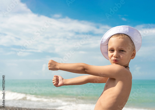 Young boy in white panama hat after swimming in the sea rests on the beach, fools around, waving your arms, rest on the beach in the summer