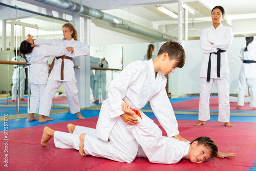 Two young boys training joint lock movement during group karate training. Their teacher standing behind and observing.