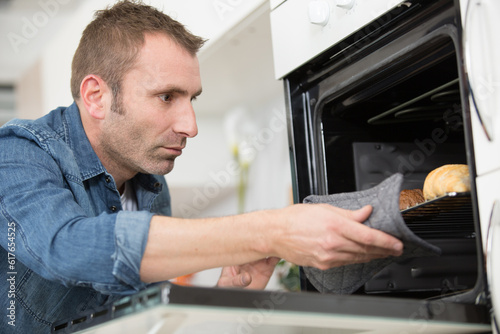man taking tray of baked croissants from oven