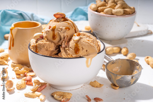 Peanut butter ice cream balls. A lot nuts gelato scoops in ceramic bowl, with caramel sauce, white kitchen background copy space